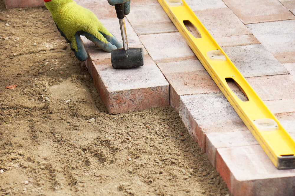 close up of a handyman gardener laying some bricks with a level laying on the bricks
