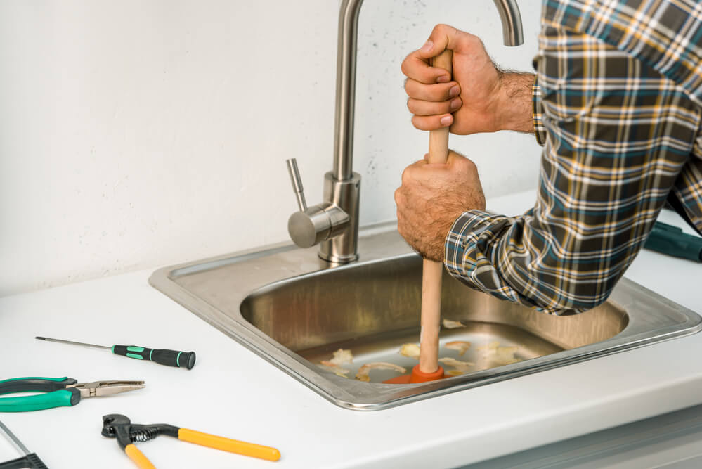 handyman cleaning out a blocked sink with a plunger and his tools on the bench
