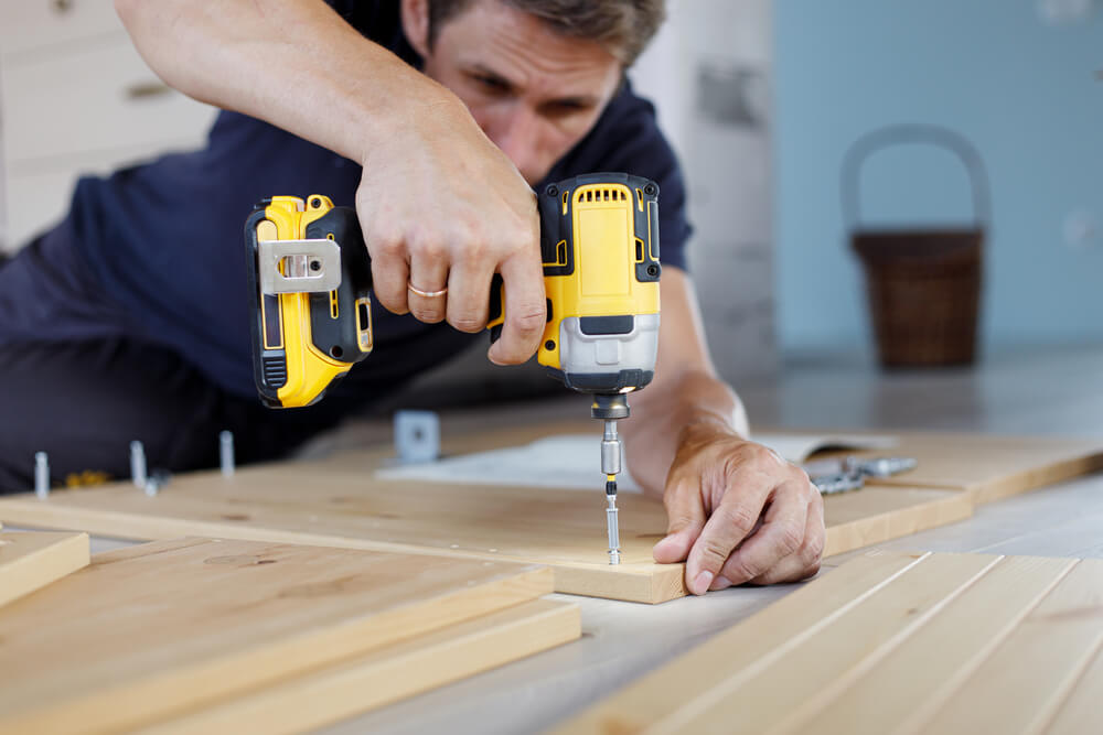 man using a drill to install a screw into a panel of a flat packed furniture piece