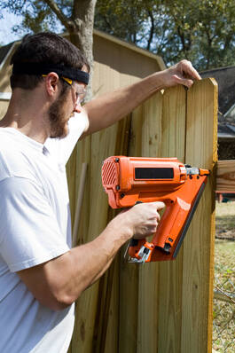 over the shoulder shot of a fence worker using a nail gun to install wooden fence planks