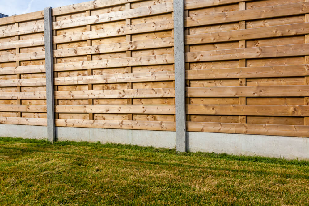 outside shot of a wooden fence with a concrete base and green grass